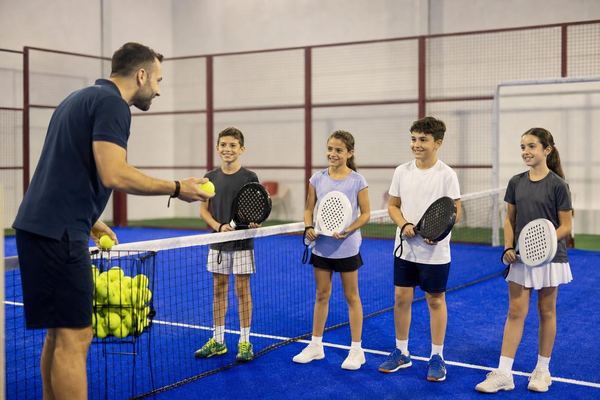 Un entrenador da clase de pádel a un grupo de niños en la pista