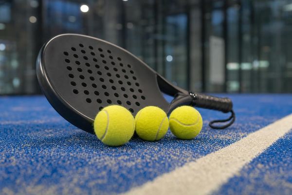 Pala de pádel y tres pelotas sobre el césped azul de una pista